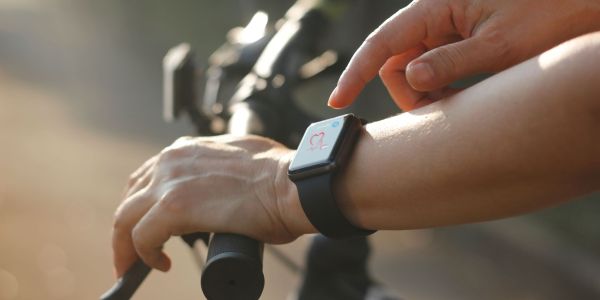 Female cyclist hands with heart rate icon on smart watch, bicycle in summer trail. All on screen are designed up.