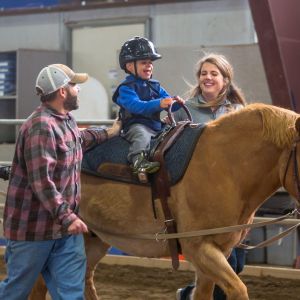 A young child rides a horse at the National Ability Center in Park City. Two volunteers walk along side him, helping with support.