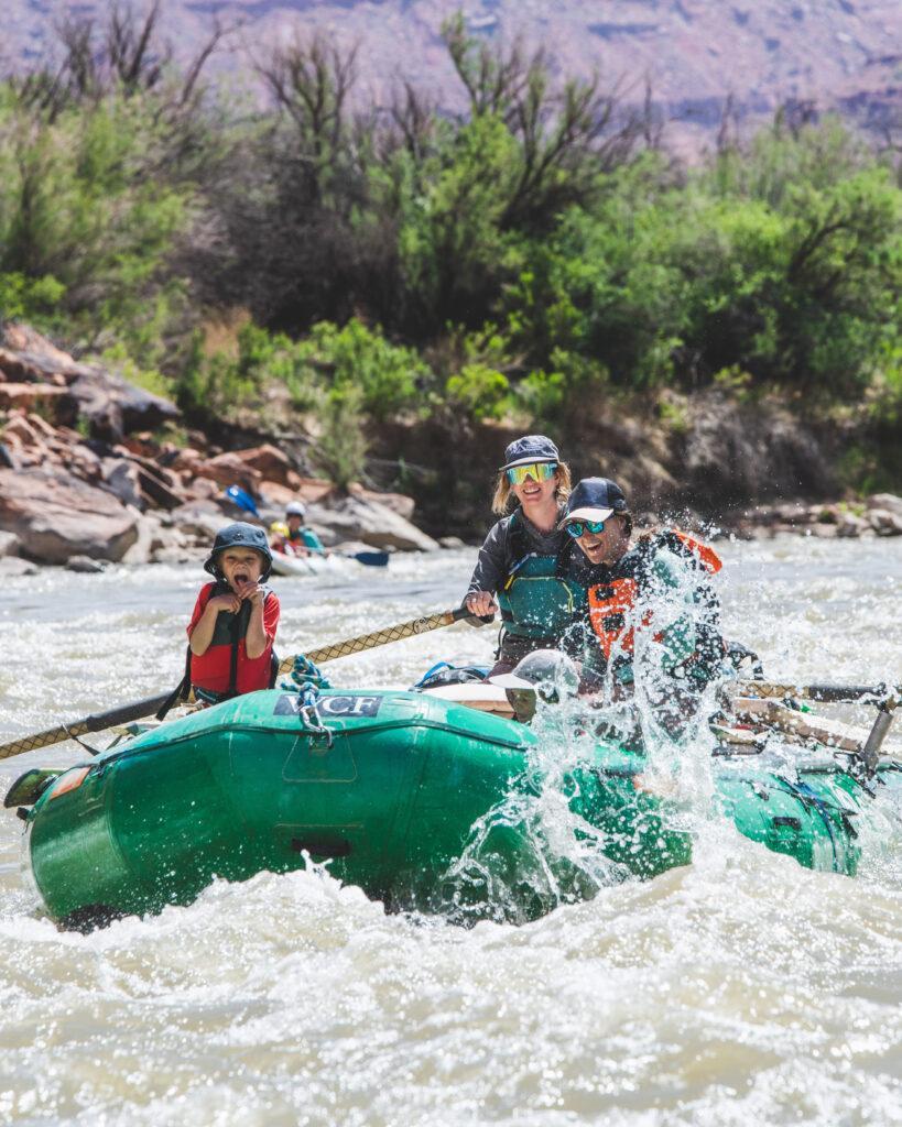 Two participants and a guide are floating down the river, with water splashing up.