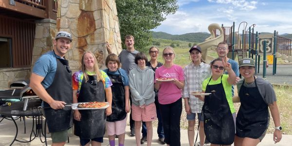 A group of young adults hold up their homemade pizzas outside of the National Ability Center in Park City, UT. The PCALL activity on this day was pizza making!