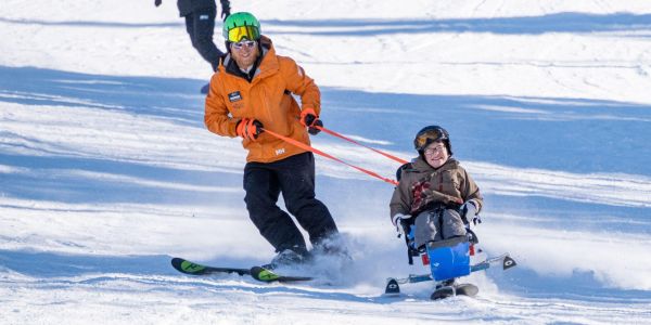 A young boy in a bi ski skis in front of an NAC instructor at Park City Mountain Resort.