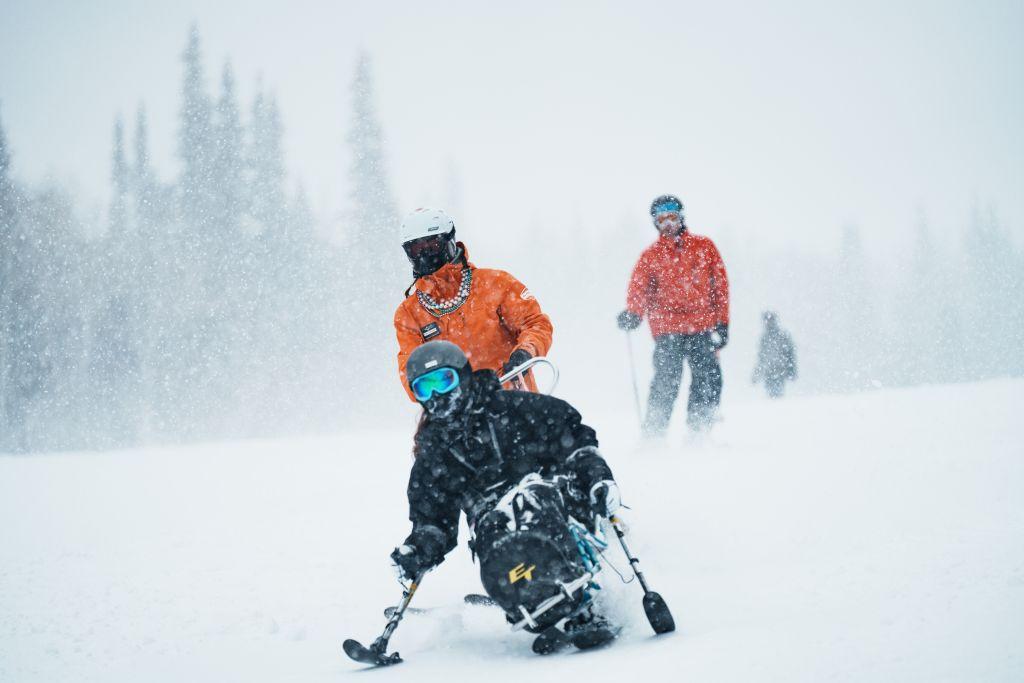 National Ability Center Participant slides on snow using a bi-ski with an instructor tethering them from behind. 