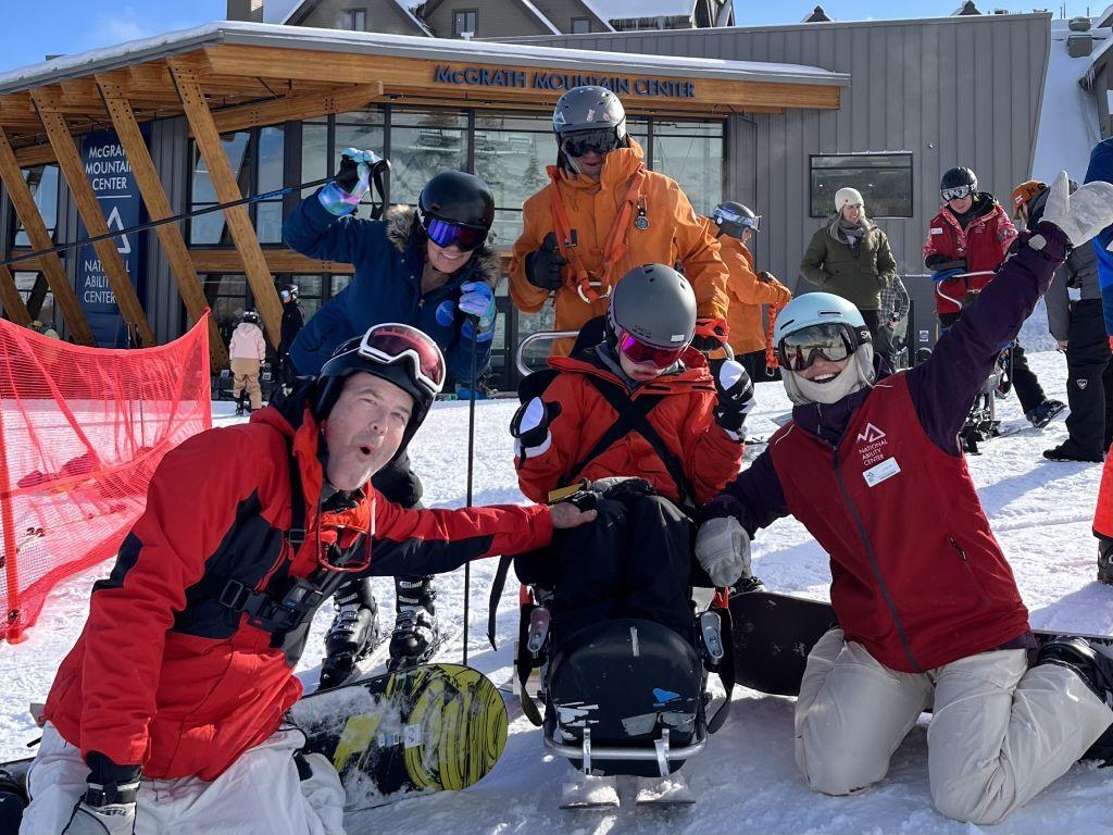 Occupational Therapy Student, pictured with a National Ability Center participant in a bi-ski and their family in front of the McGrath Mountain Center at Park City Mountain Resort. 