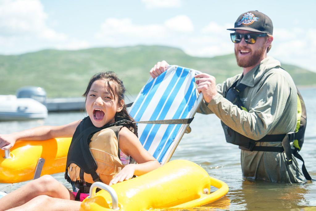 A young girl with a disability laughs while floating in an adaptive floating chair in the Jordanelle Reservoir. 